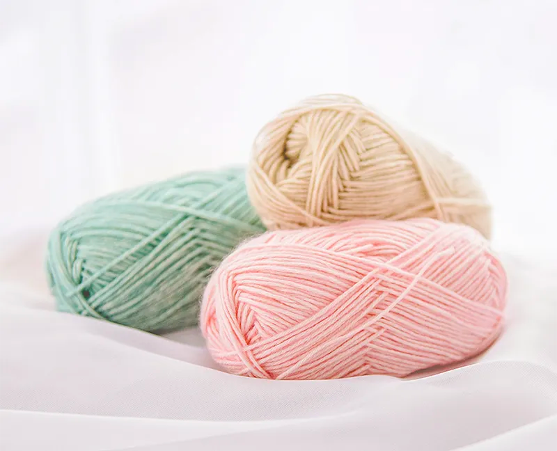 Three balls of yarn in pastel colors on a white background