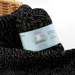 KnitPal GentleBliss DK weight yarn in black with multicolor marl flecks, two skeins on knitted fabric swatch, label visible