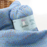 KnitPal GentleBliss DK weight yarn in periwinkle blue with multicolor marl flecks, skein on knitted fabric swatch, label visible