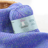 KnitPal GentleBliss DK weight yarn in periwinkle violet with multicolor marl flecks, skein on knitted fabric swatch, label visible