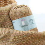 KnitPal GentleBliss DK weight yarn in warm camel brown with multicolor marl flecks, skein on knitted fabric swatch, label visible