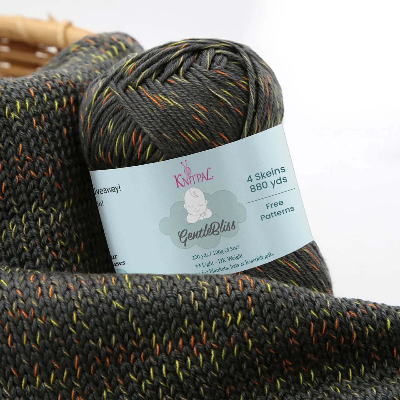 KnitPal GentleBliss DK weight yarn in charcoal gray with orange and yellow-green marl flecks, skein on knitted fabric swatch, label visible