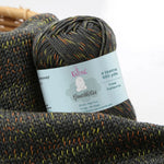 KnitPal GentleBliss DK weight yarn in charcoal gray with orange and yellow-green marl flecks, skein on knitted fabric swatch, label visible