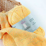 KnitPal GentleBliss DK weight yarn in soft sunny yellow with multicolor marl flecks, skein on knitted fabric swatch, label visible