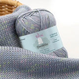 KnitPal GentleBliss DK weight yarn in soft silver gray with multicolor marl flecks, skein on knitted fabric swatch, label visible