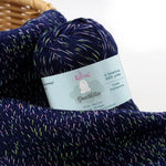 KnitPal GentleBliss DK weight yarn in rich navy blue with multicolor marl flecks, skein on knitted fabric swatch, label visible