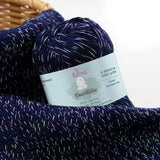KnitPal GentleBliss DK weight yarn in rich navy blue with multicolor marl flecks, skein on knitted fabric swatch, label visible