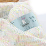 KnitPal GentleBliss DK weight yarn in white with soft pastel pink, yellow, and blue marl flecks, skein on knitted fabric swatch, label visible