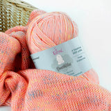 KnitPal GentleBliss DK weight yarn in warm coral peach with multicolor marl flecks, skein on knitted fabric swatch, label visible
