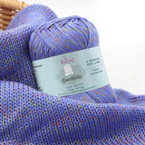KnitPal GentleBliss DK weight yarn in vibrant periwinkle purple with orange and yellow-green marl flecks, skein on knitted fabric swatch, label visible