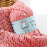 KnitPal GentleBliss DK weight yarn in fresh coral pink with multicolor marl flecks, skein on knitted fabric swatch, label visible