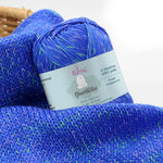 KnitPal GentleBliss DK weight yarn in bold royal blue with green and pink marl flecks, skein on knitted fabric swatch, label visible