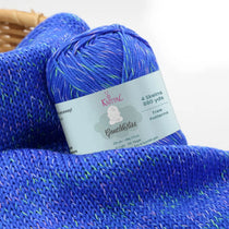 KnitPal GentleBliss DK weight yarn in bold royal blue with green and pink marl flecks, skein on knitted fabric swatch, label visible