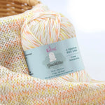 KnitPal GentleBliss DK weight yarn in creamy white with orange and yellow marl flecks, skein on knitted fabric swatch, label visible
