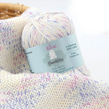 KnitPal GentleBliss DK weight yarn in crisp white with pink and lavender marl flecks, skein on knitted fabric swatch, label visible